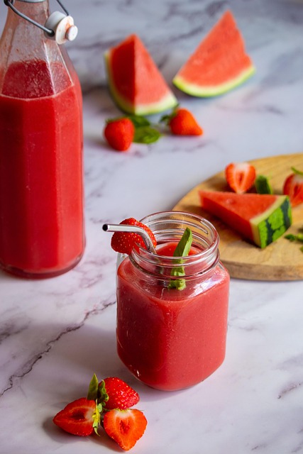 Une image d'un smoothie à la fraise et pastèque, servi dans un verre avec une paille. Des tranches de pastèque et des fraises fraîches sont disposées autour.